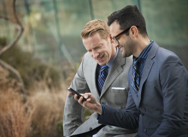 Two men standing side by side,looking at a cell phone screen or mobile phone.
